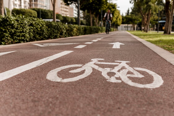 rote Fahrbahn mit einem aufgezeichneten Fahrrad, im Hintergrund ein Fahrradfahrer